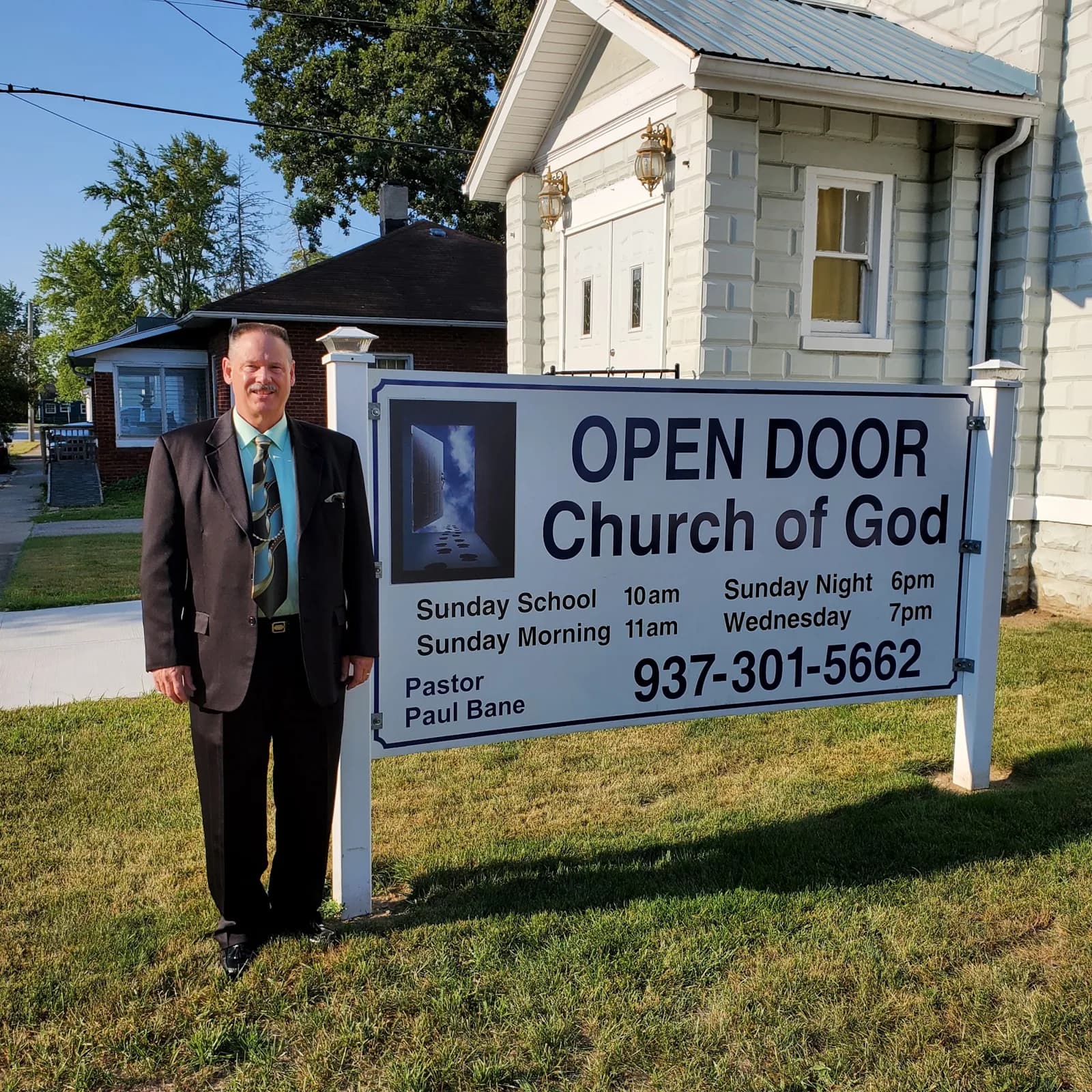 Pastor Paul Bane standing beside the Open Door Church of God sign