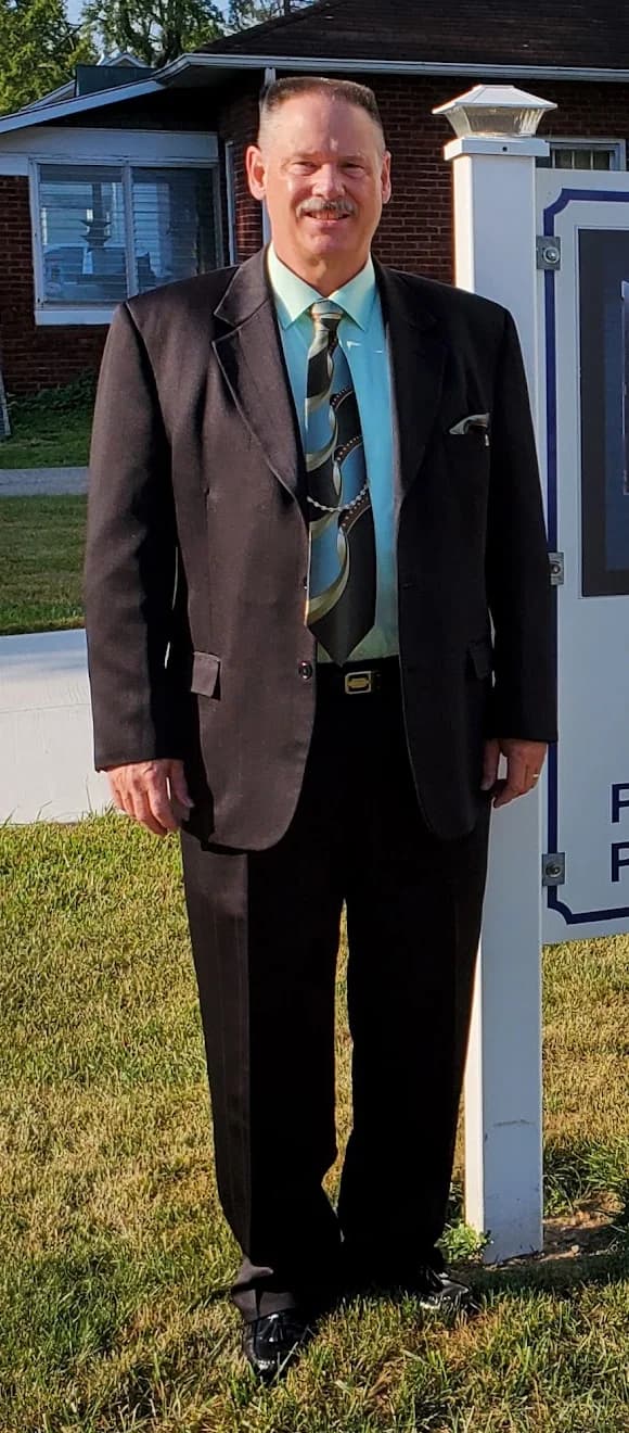 Pastor Paul Bane standing on the church lawn in a dark suit and tie