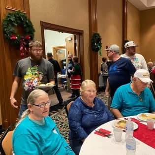 Church members sharing a meal at round tables decorated for Christmas